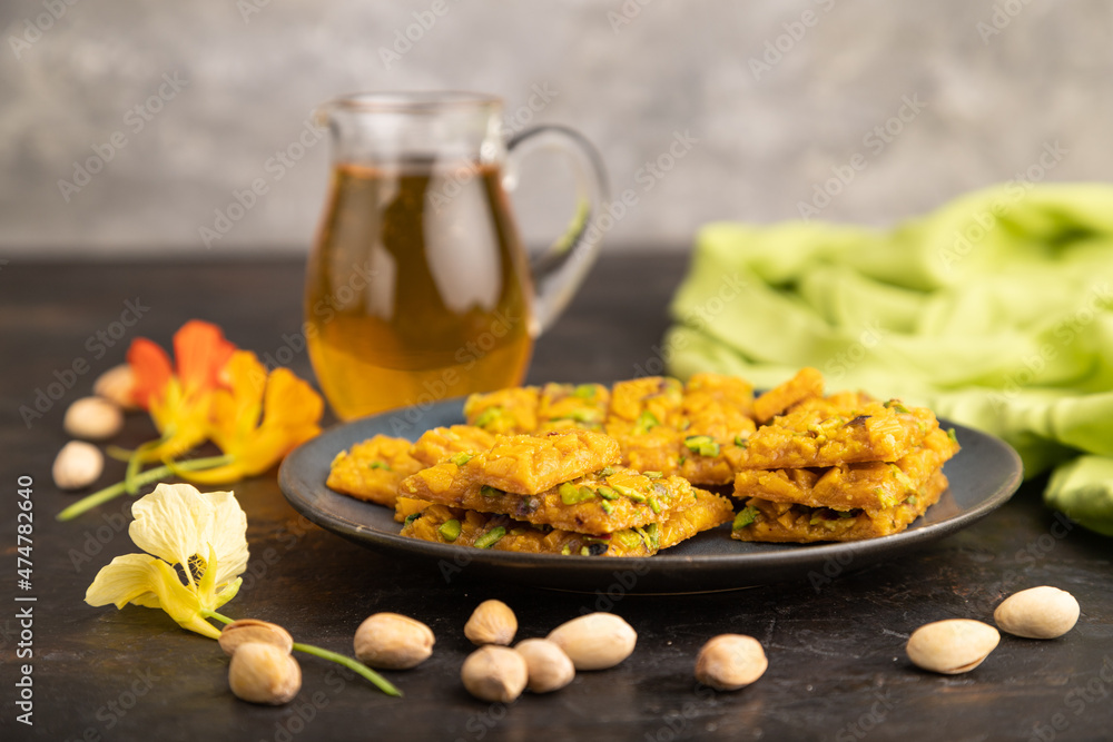 Traditional iranian dessert sohan with glass of green tea on a black concrete background. side view, close up. Traditional iranian dessert sohan with glass of green tea on a black concrete background. side view, close up.