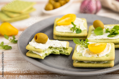 Green cracker sandwiches with cream cheese and cherry tomatoes on white wooden background. side view, selective focus.