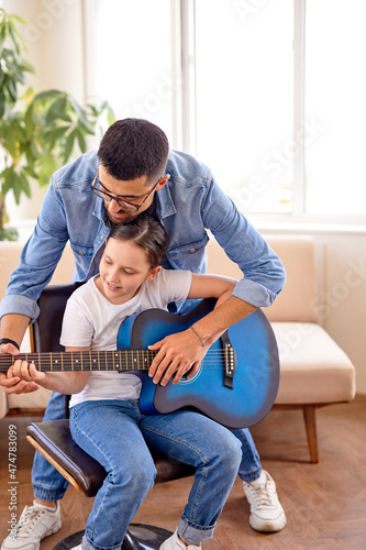 pretty girl and man hold guitar learning new chord, spend weekend time at home indoors, in bright cozy room, caucasian child girl with teacher in casual wear, performing music together, larn new song