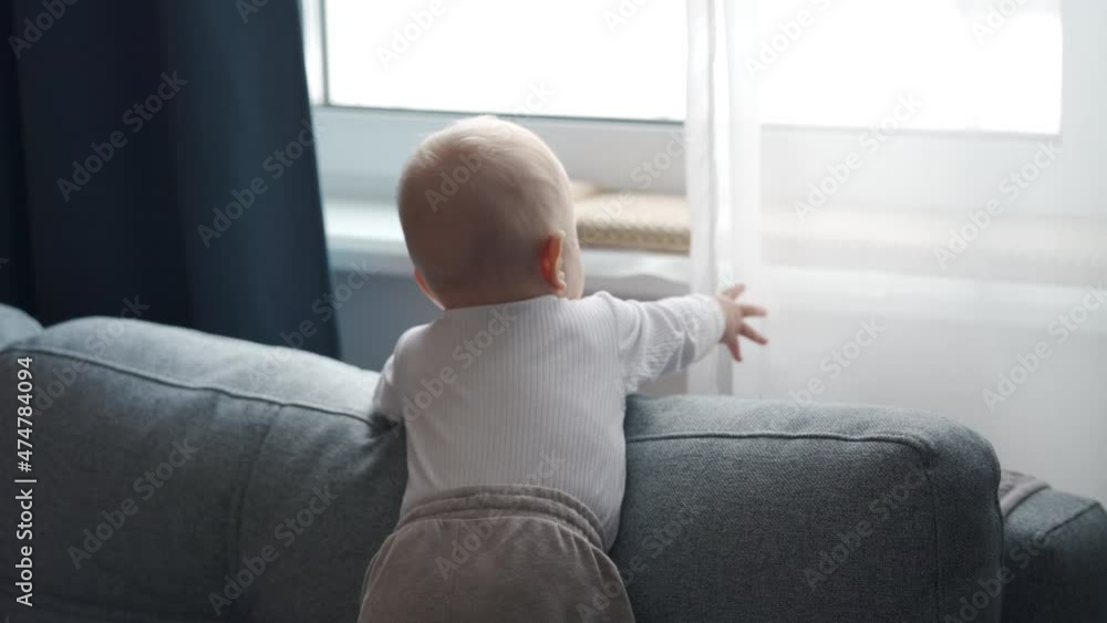 Cute baby boy standing by the window of apartment looking out the window at the street, child is waiting at home. High quality 4k footage Cute baby boy standing by the window of apartment looking out the window at the street, child is waiting at home. High quality 4k footage
