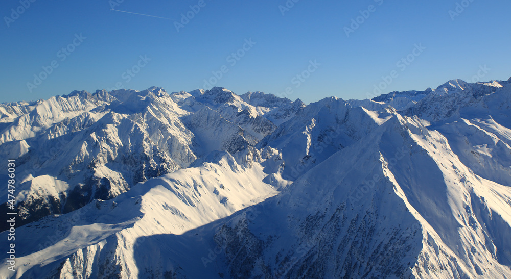survol, vue d'avion d'une superbe chaine montagneuse enneigé sous le soleil avec un ciel bleu 