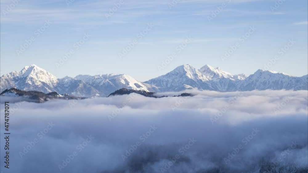 Low inversion clouds moving in alpine valley. Time lapse of fog covering amazing landscape in winter. Snowy mountains in the distance. Pristine nature in Slovenia, Europe. Sunrise. Static shot Low inversion clouds moving in alpine valley. Time lapse of fog covering amazing landscape in winter. Snowy mountains in the distance. Pristine nature in Slovenia, Europe. Sunrise. Static shot