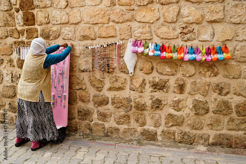 A woman in traditional clothing and with her head covered displays handmade jewelry and crocheted items for sale on a stone wall in Midyat, Eastern Anatolia, Turkey. photo