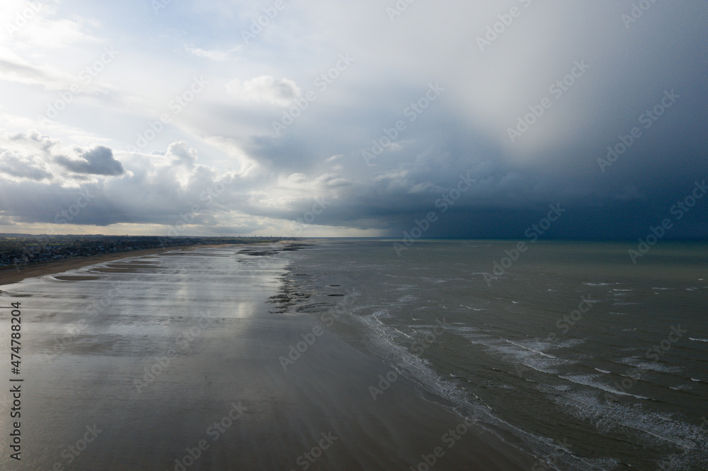 The thunderstorm over the long sandy beach at the edge of the Channel Sea in Europe, France, Normandy, Ouistreham, in summer, on a sunny day.