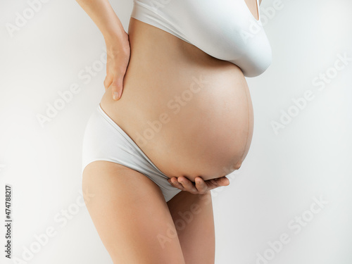 Lady in the third trimester of pregnancy. A pregnant woman in white underwear grabbed her belly and lower back white background. The girl in the last month of pregnancy feels heaviness and strain on photo