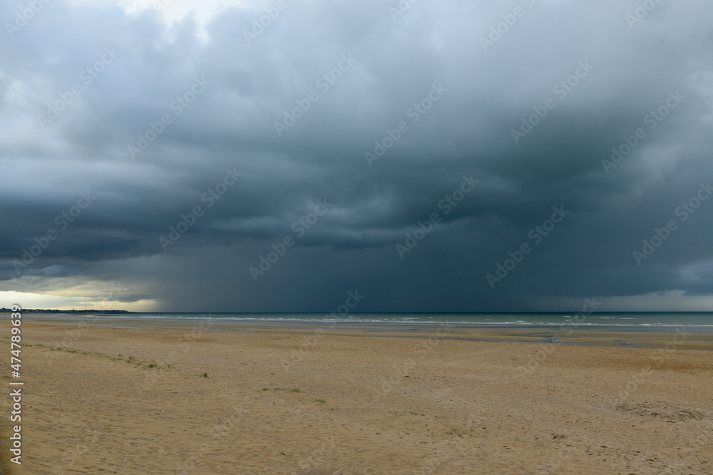A downpour over the English Channel and Ouistreham beach in Europe, France, Normandy, in summer, on a sunny day.