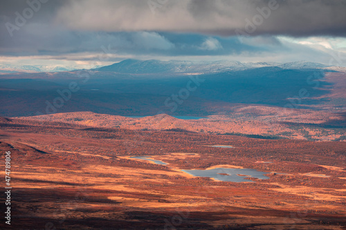 Landscape of Pieljekaise National Park in autumn with lakes and snowy mountains in Lapland in Sweden, colored plants, dramatic light and clouds in sky.