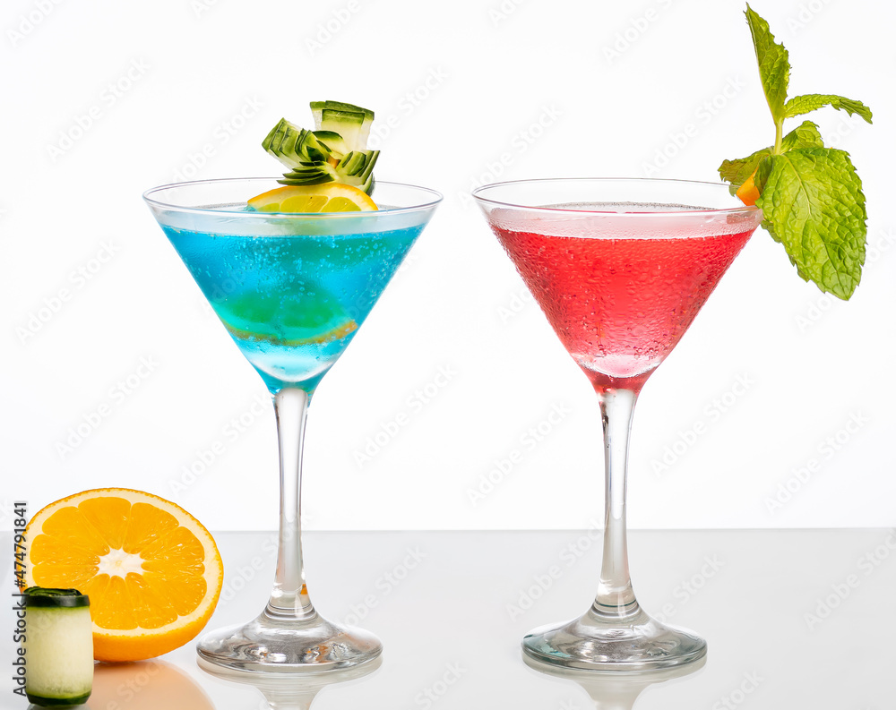 one glass of blue cocktail and one with red cocktail, on reflective surface, isolated on white background.