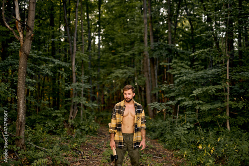 Logging season. Confident Caucasian Lumberman carry axe in forest, sexy handsome woodman. Forestry logging. Chopping wood. Summer nature. Natural landscape. Ecology and environment. Lumberjack © Roman