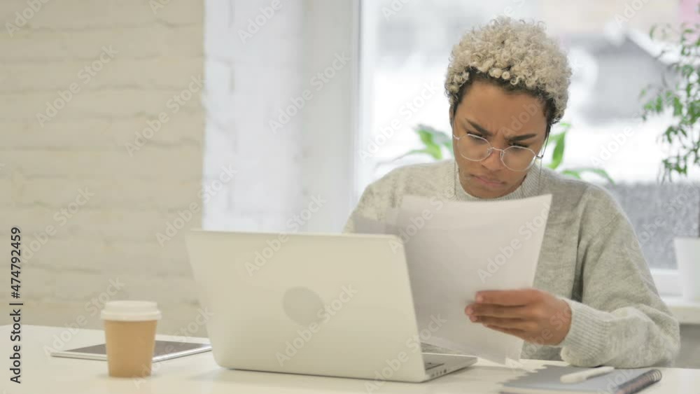 African Woman with Laptop Upset while Reading Documents in Office African Woman with Laptop Upset while Reading Documents in Office