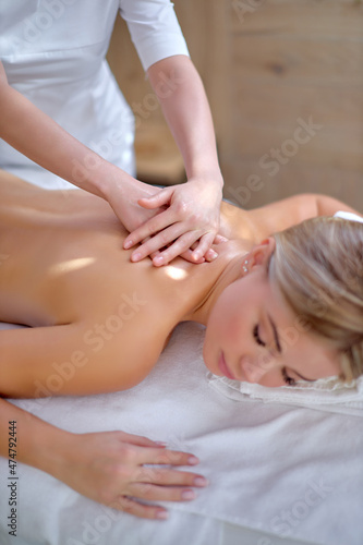 Pretty caucasian blonde Woman enjoying relaxing back massage in cosmetology spa centre, lying on massage couch. Body care, skin care, wellness, wellbeing, beauty treatment concept.