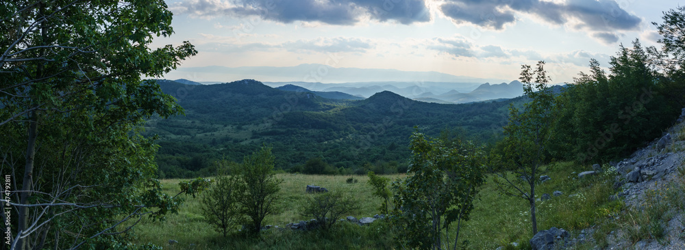 Panorama of mountain scene during sunny day with meadow in foreground, Croatia