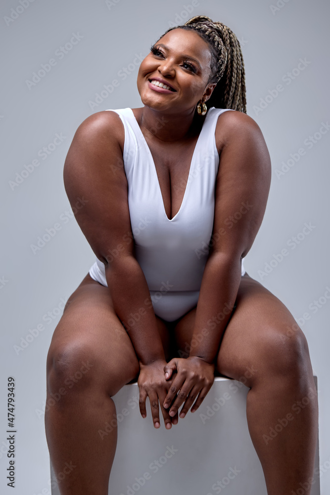 Excited plus size black woman in white bodysuit laughing, sitting in studio  over white background, rejoicing. Concept of body positive, equality,  people diversity. copy space, free space. portrait Stock Photo | Adobe