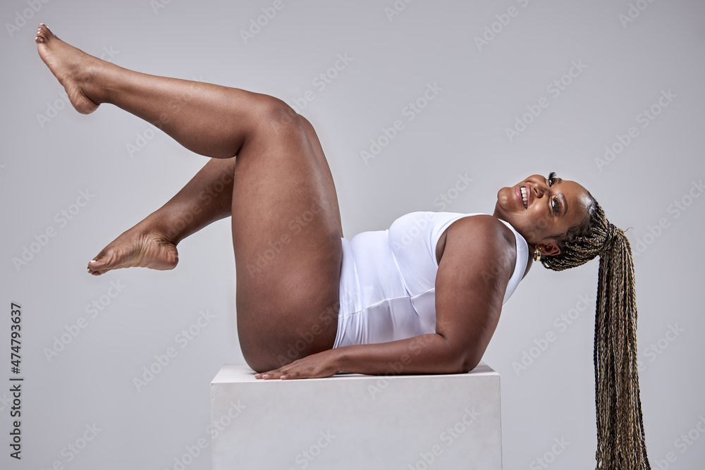 Foto Stock Plus size sexy happy feminine model in white beautiful bodysuit  posing on cube, fat woman isolated on white studio background enjoy having  overweight body, body positive and beauty concept.