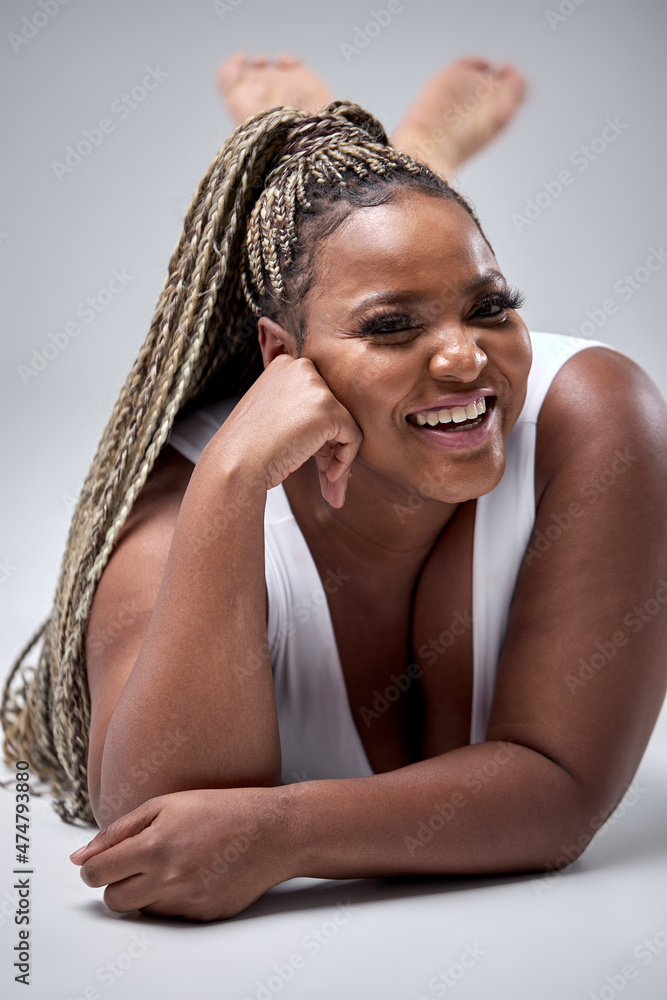 Fototapeta premium Gorgeous plus size or plump black woman enjoying her natural body. beautiful female model in white bodysuit posing against gray background. Lifestyle portrait. human emotions, beauty, diversity