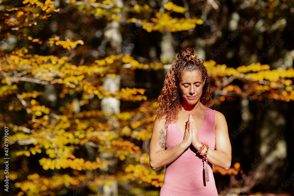 Latin woman with her hands together and eyes closed meditating in the forest during fall. Latin woman with her hands together and eyes closed meditating in the forest during fall.