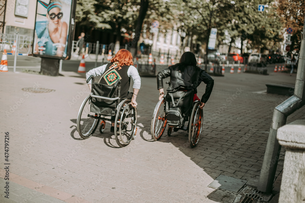 Two girls in wheelchairs near an advertising banner with a smiling girl. Women with special need walk around Kiev near Khreshchatyk and admire the sights. Happy girl on a wheelchair with her friend Two girls in wheelchairs near an advertising banner with a smiling girl. Women with special need walk around Kiev near Khreshchatyk and admire the sights. Happy girl on a wheelchair with her friend