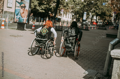 Two girls in wheelchairs near an advertising banner with a smiling girl. Women with special need walk around Kiev near Khreshchatyk and admire the sights. Happy girl on a wheelchair with her friend