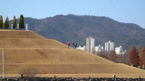 Visitors strolling up the Bonghwa Hill on a spiral road in Lake Garden of Suncheonman Bay National Garden with Suncheon city buildings and mountains on background photo