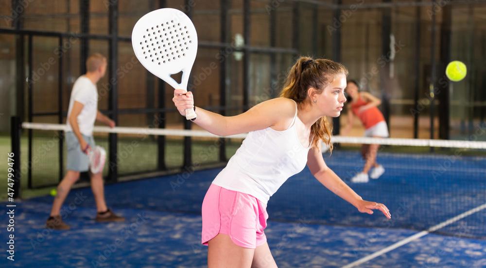 Young sporty woman padel player hitting ball with a racket on a hard court