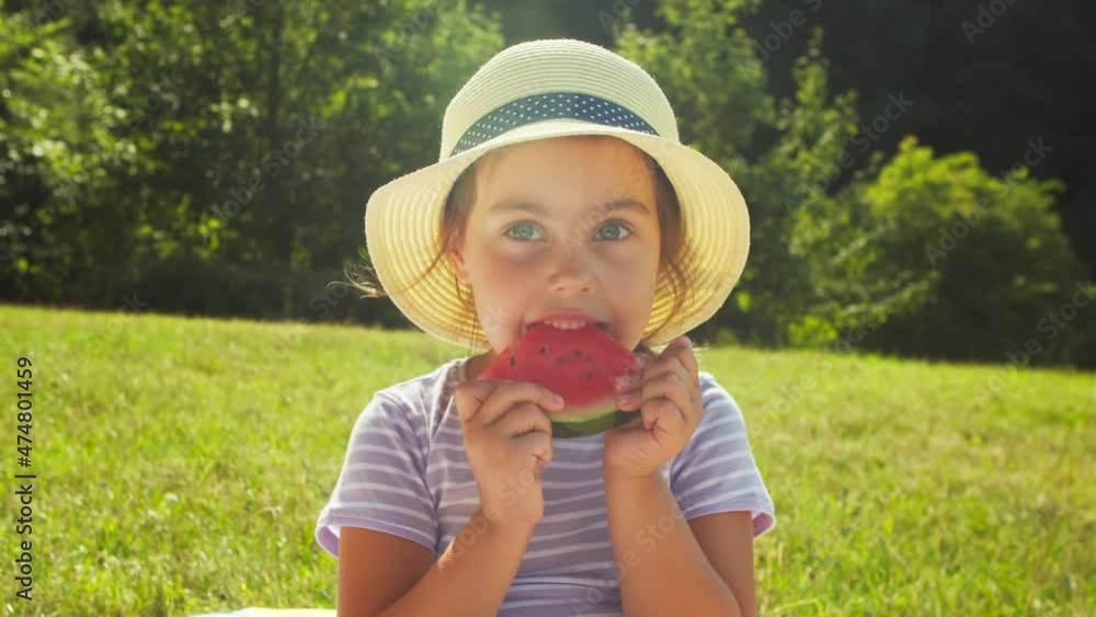 Preschool girl in a headdress has a watermelon in the park in the summer on a picnic. Cute little girl is eating a juicy watermelon lying on the grass in a clearing in the forest on a sunny summer day Preschool girl in a headdress has a watermelon in the park in the summer on a picnic. Cute little girl is eating a juicy watermelon lying on the grass in a clearing in the forest on a sunny summer day