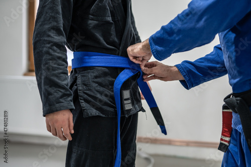 BJJ brazilian jui jutsu belt promotion close up on hands of unknown instructor black belt professor tie up blue belt on waist of his student photo