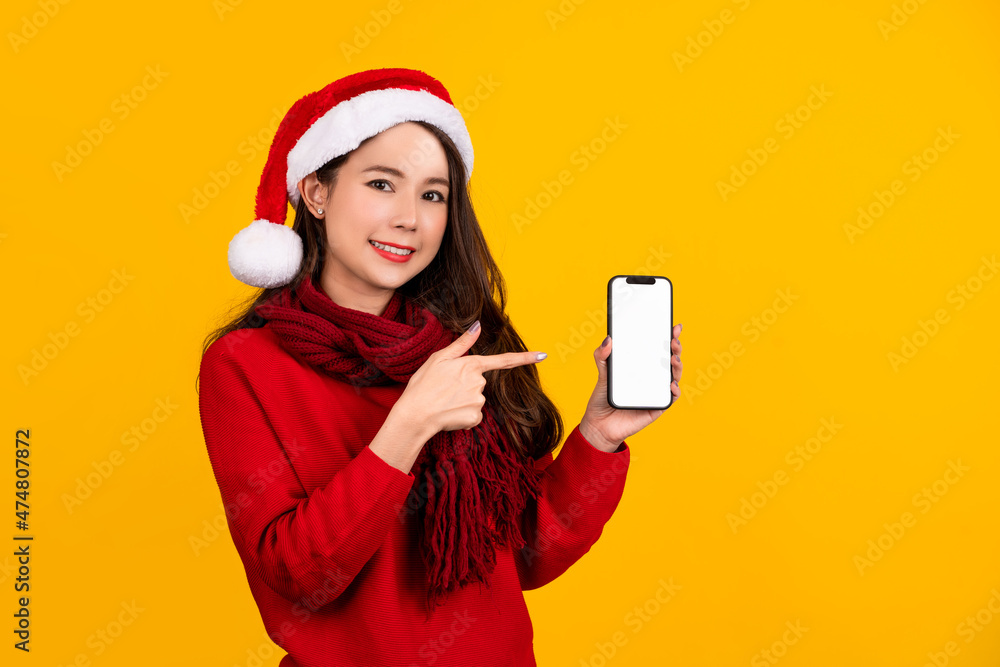Smiling young Santa woman in sweater, Christmas hat hold mobile cell phone with blank empty screen isolated on yellow background. Smiling young Santa woman in sweater, Christmas hat hold mobile cell phone with blank empty screen isolated on yellow background.