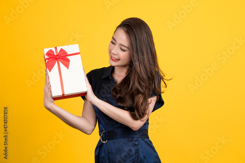 A young brunette girl with a beautiful wide smile holds a surprise gift for the special holiday in her hands. New Year, Christmas and Valentines Day concept
