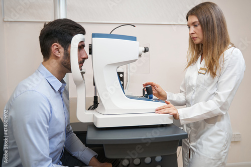 Woman oculist controlling autorefractor while checking patient eyesight photo