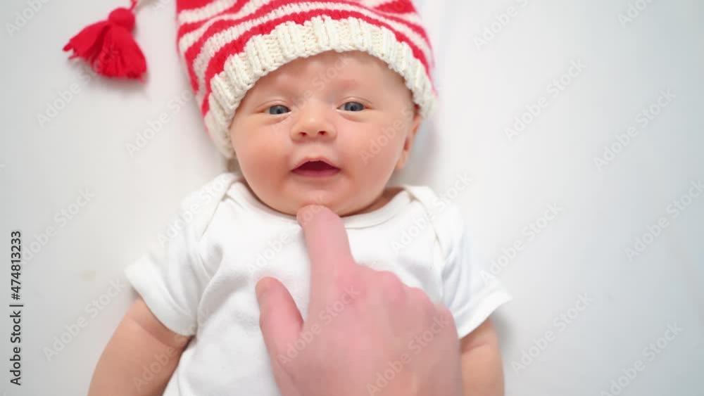 hand touches face of cute little kid in cap of Christmas elf or gnome.baby santa hand touches face of cute little kid in cap of Christmas elf or gnome.baby santa