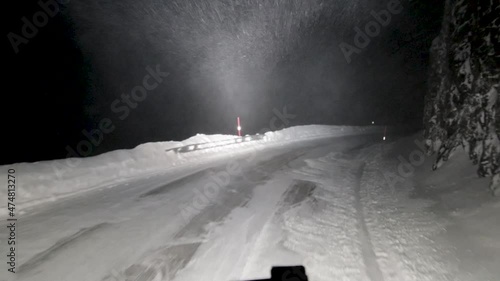 POV shot of a Truck driver traveling along a treacherous mountain pass covered in snow and ice, the falling snow affecting night time visibility as he cautiously drives along the road, Soroya, Norway photo