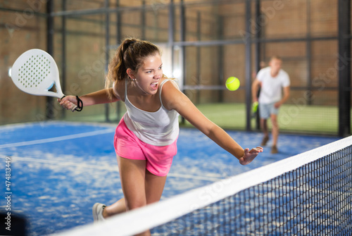Young beautiful woman in white t-shirt playing padel tennis indoor © JackF