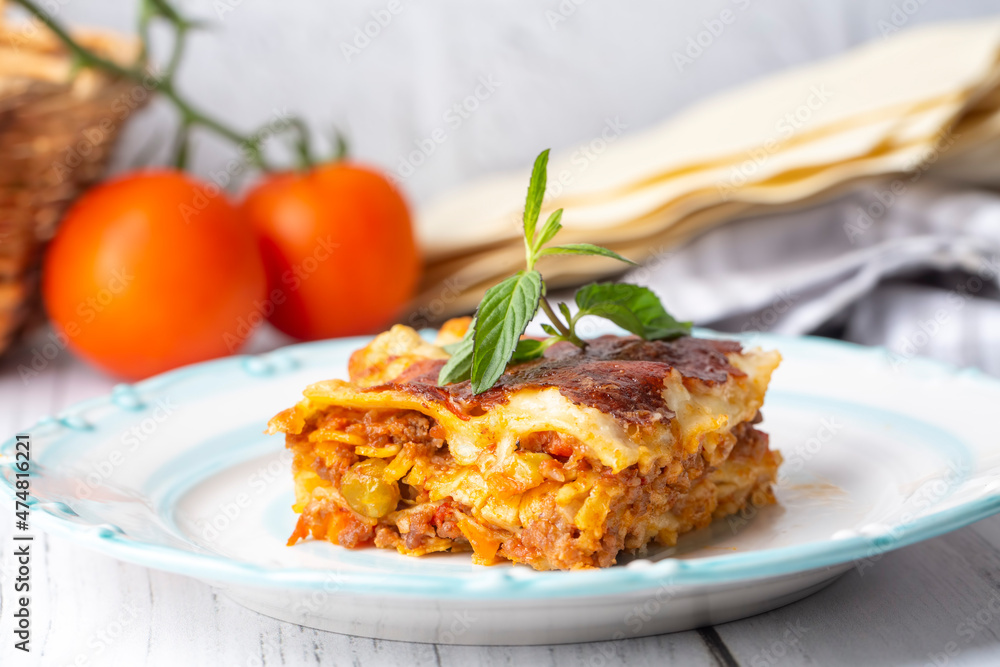 Piece of tasty hot lasagna served with a basil leaf on a gray plate. Italian cuisine, menu, recipe. Homemade meat lasagna. Close up, side view Piece of tasty hot lasagna served with a basil leaf on a gray plate. Italian cuisine, menu, recipe. Homemade meat lasagna. Close up, side view