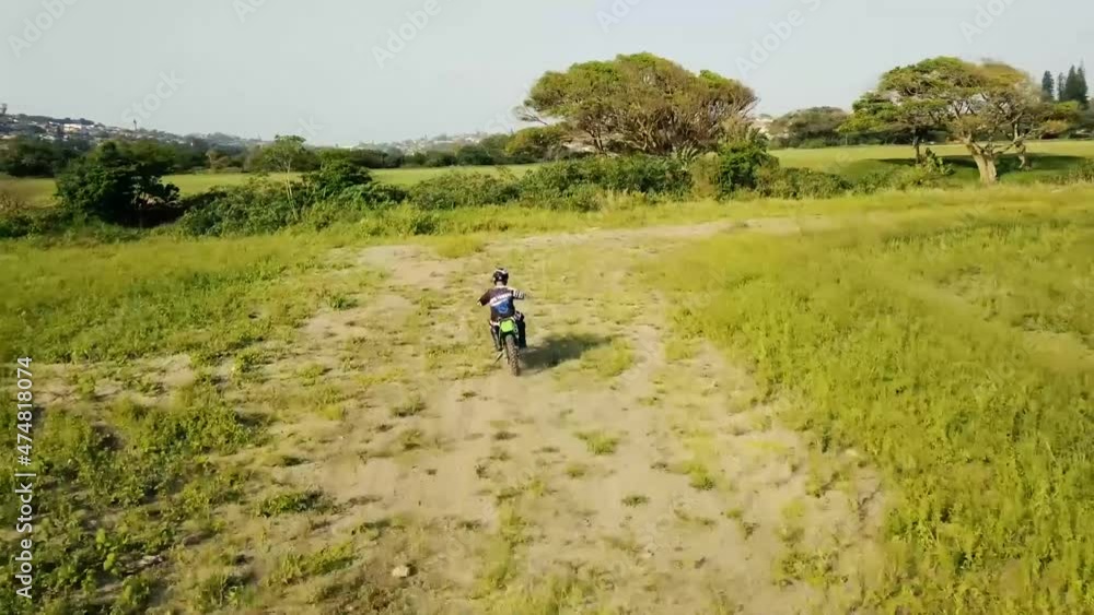Person riding a green motorcycle in a dirt field area enduro off road riding with a drone following from above and behind. Person riding a green motorcycle in a dirt field area enduro off road riding with a drone following from above and behind.