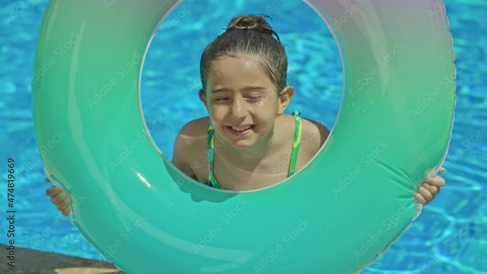 Little girl in swimsuit with inflatable rubber ring in swimming pool ...