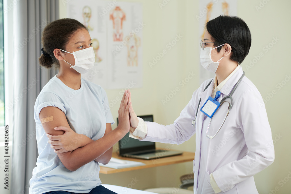 Teenage girl in medical mask giving high five to doctor after getting shot of vaccine against coronavirus Teenage girl in medical mask giving high five to doctor after getting shot of vaccine against coronavirus