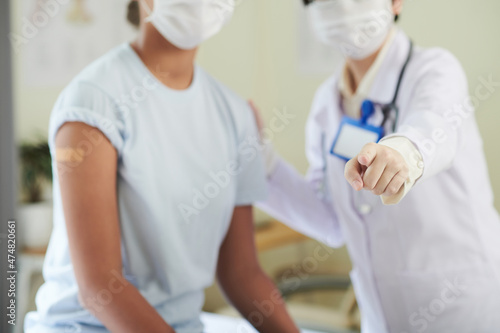 Doctor standing next to teenage girl who just got vaccine against coronavirus and pointing at camera © DragonImages