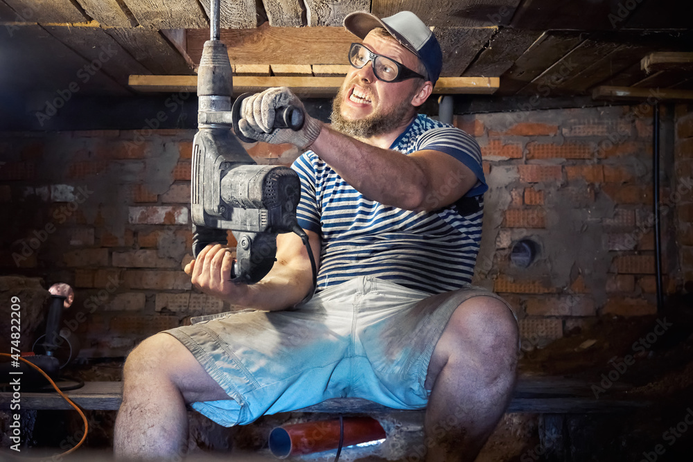 Fototapeta premium Funny bearded man with heavy duty perforator in the basement of the house