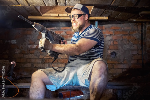 Fototapeta Naklejka Na Ścianę i Meble -  Funny bearded man with heavy duty perforator in the basement of the house