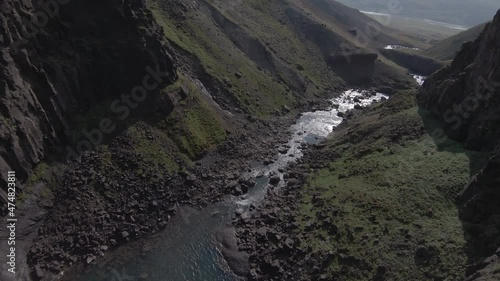 Dive bombing past waterfall in Iceland canyon with bright sunlight, FPV Shot