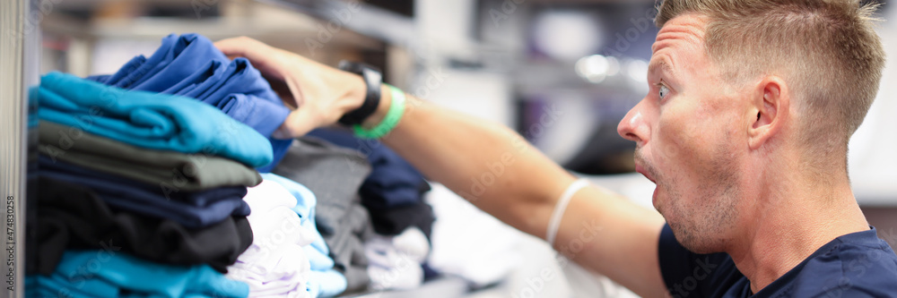 Surprised man looks at shelf with clothes in store closeup