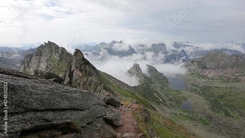 Unusual mountains with steep limestone slopes over gentle green hills. The steep stone ledge at the top is covered with clouds. Shooting from a bird's eye view from a quadcopter