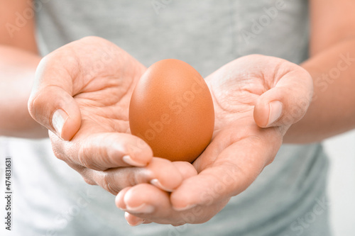 Close-up of a Young Woman wearing a gray T-shirt at her home holding a brown chicken egg with her hand in the morning. Shoot over white background. Natural healthy food and organic farming concept
