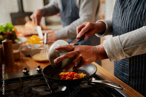 Hands of multi-cultural elderly couple cooking healthy breakfast together in modern kitchen at stove.