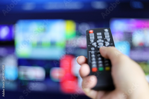 Remote controller in female hand on smart TV screen background. Woman choosing streaming services, watching movies