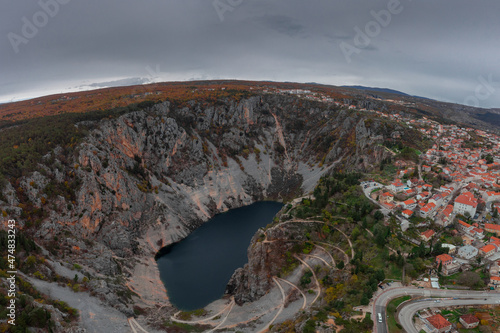 Fotografie, Obraz Blue lake, a large sinkhole close to more known Red lake at the edge of village of Imotski in southern Croatia on a gray day