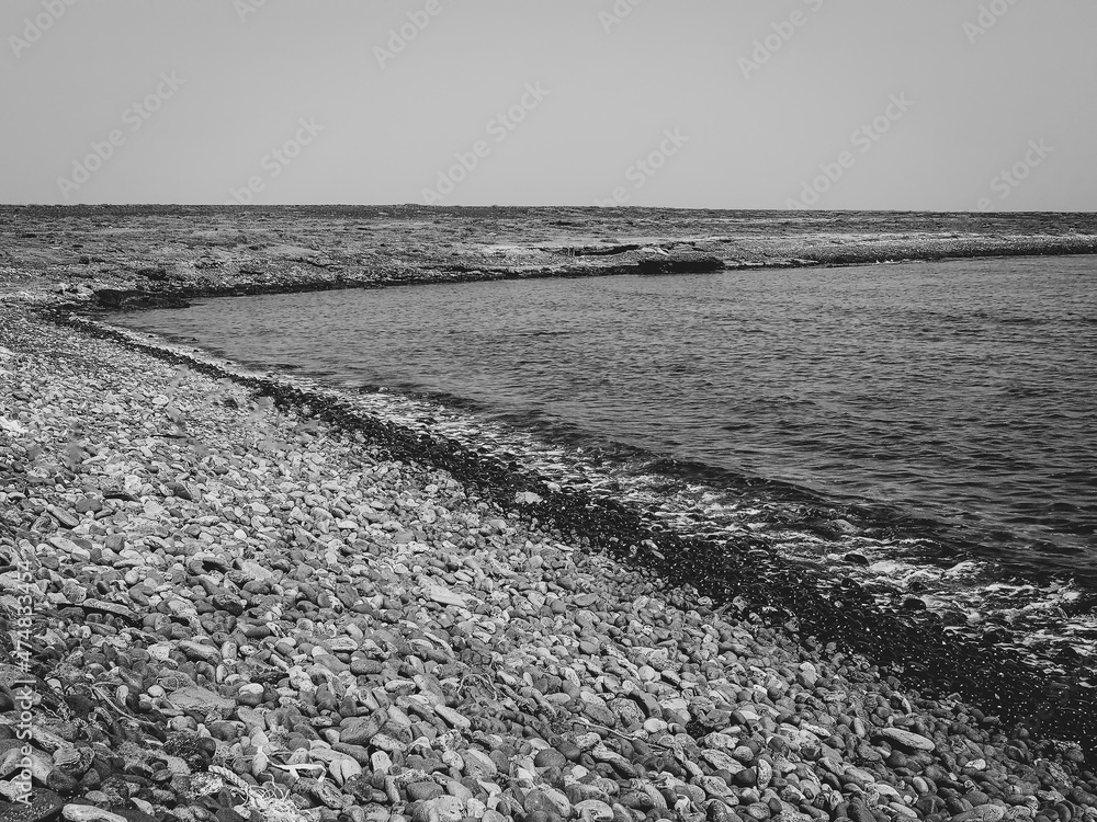 Monochrome pebble beach in Cape Verde. Calm Atlantic Ocean water in a small lagoon, large stones on the shore. Selective focus on the details, blurred background.