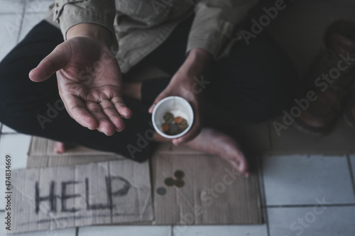 Homeless adult man sitting on the street in the shadow of the building and begging for help and money with sign. Homeless concept..