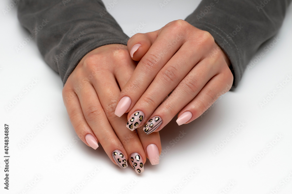 New Year's leopard manicure. Black, gold, beige manicure on long narrowed square nails close-up on a white background. Hands with a gray sweater. New Year's leopard manicure. Black, gold, beige manicure on long narrowed square nails close-up on a white background. Hands with a gray sweater.