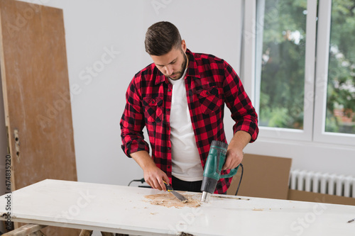 man removing old paint from door with heat gun